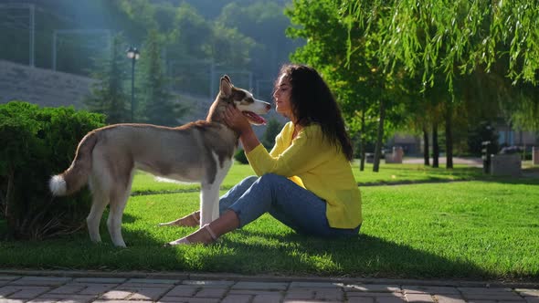 Young Woman with Her Adult Husky Dog are Resting in Park at Sunny Morning