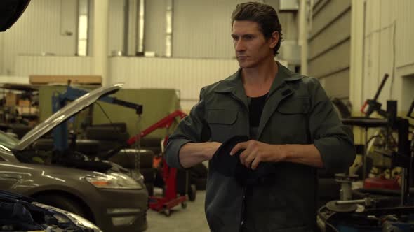 Video shot of the serious adult auto mechanic walking through the garage and wiping his hands