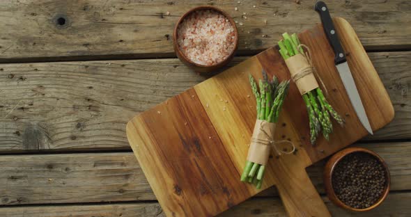 Video of two fresh asparagus bundles on wooden chopping board with knife and salt and pepper