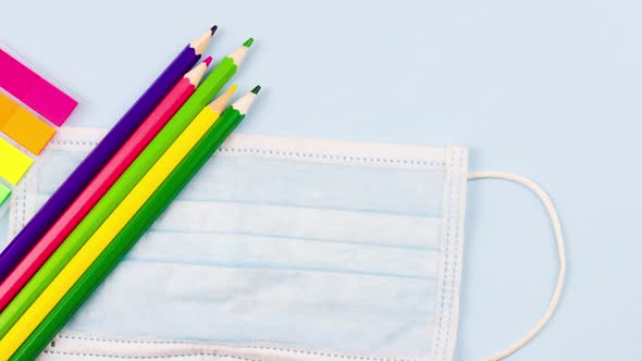 School Supplies with a Notepad Lie on a Pastel Blue Background with a Medical Mask