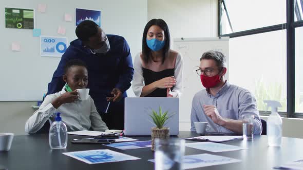 Office colleagues wearing face masks using laptop together in meeting room at modern office