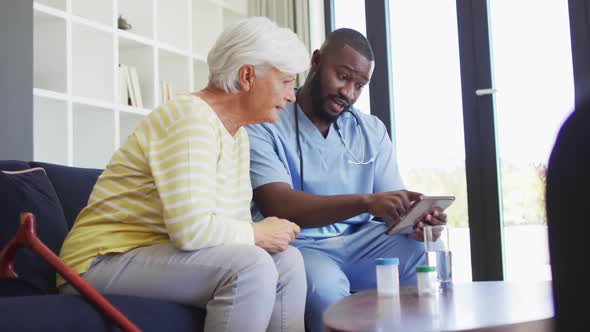 Video of african american male doctor using tablet with caucasian senior woman