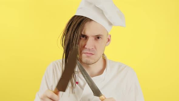 Young Serious Man Dressed As Chef with Knives on Yellow Background