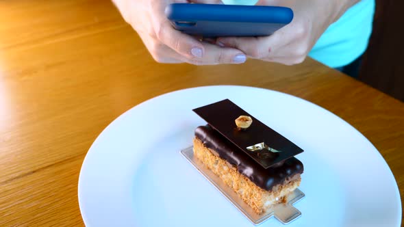 Woman Hand with Mobile Phone Take Picture of Opera Cake Dessert on White Plate