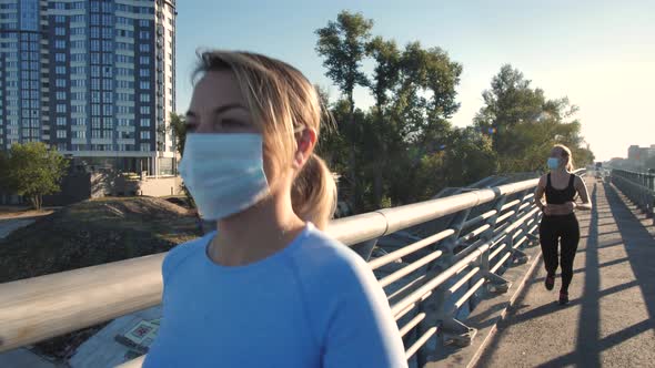 Masked Fitness Women Running Along City Bridge
