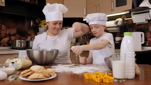 Happy Mother and Little Son in Aprons and Chef's Hats Cook Cookies Together