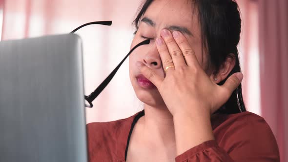 Serious Asian woman feeling tired and eyestrain after long hours working on laptop computer.