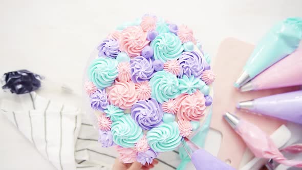Flat lay. Piping pastel color buttercream rosettes on a white cake to make a unicorn cake.