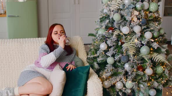 Woman Sitting on Sofa Near Christmas Tree and Drinking Alcoholic Beverage