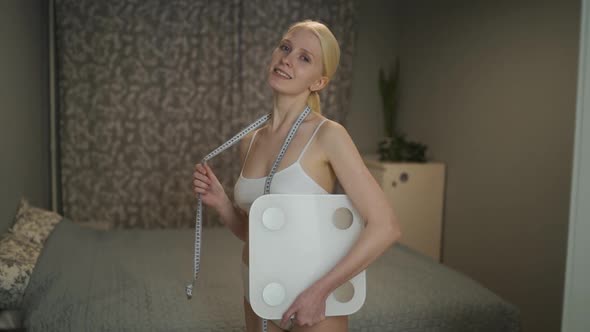 Young Slender Woman with a Measuring Tape Around Her Neck and Weights in Her Hands Posing