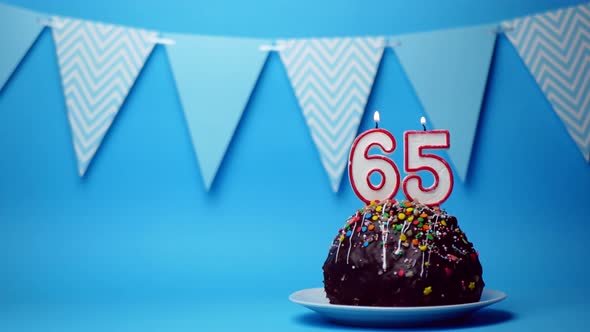 chocolate birthday cake with a burning candle number sixty five, 65 on a blue background. Copy space
