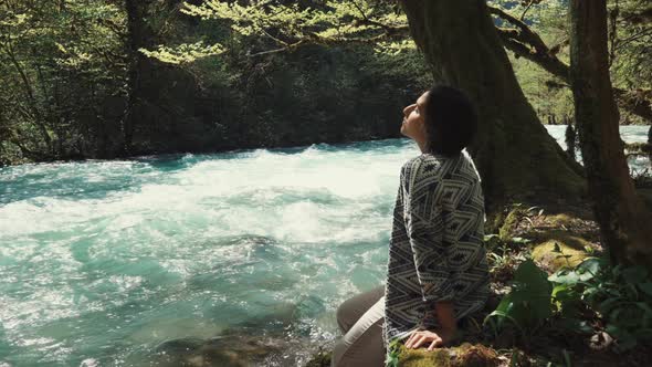 Lonely Teenager Girl Is Sitting on Ground in Woodland and Watching River Stream