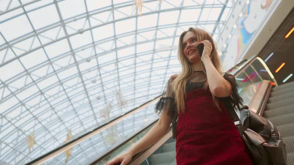 Young Smiling Woman in Blue T-shirt Standing in Shopping Center Using Smartphone, Browsing, Reading