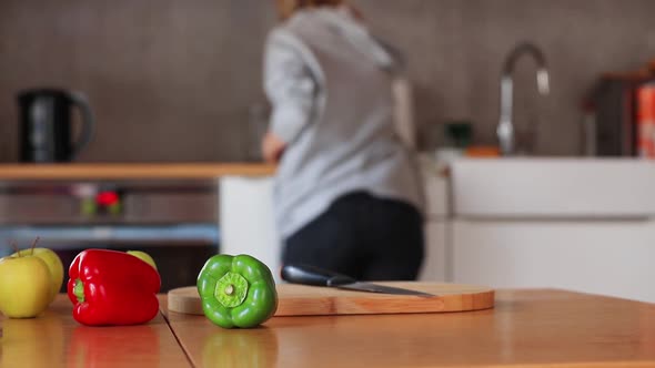 Green and red peppers with apple an knife on a wooden table with housewife on background