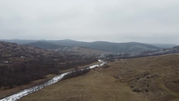 Drone shot of the forest and a country icy river in the late autumn. Late Autumn forest hills. Aeria