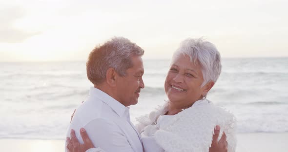 Portrait of happy hispanic just married senior couple embracing on beach at sunset