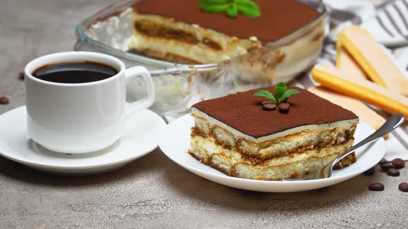 Traditional Italian Tiramisu dessert in glass baking dish and portion on grey concrete background