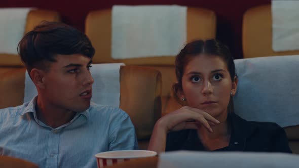 young caucasian couple using smartphone while watching film in movie theater.