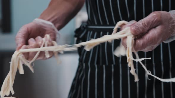 A Man in Gloves Holds Pieces of Cheese and Stretches Them