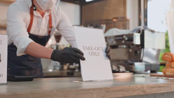 Asian cafe business owner wear face mask and shield, put TAKE OUT ONLY sign on coffee bar counter