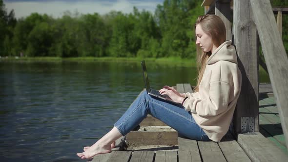 Young Girl Student Doing Homework Studying with Laptop Outdoors on Peaceful Lake