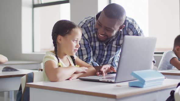 Video of happy african american male teacher helping caucasian girl with laptop