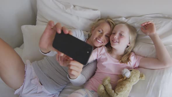 Ovear head view of Caucasian woman and her daughter taking selfie on bed