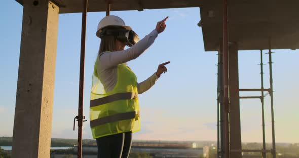 Woman Inspector in VR Glasses and Helmet Checks the Progress of the Construction of a Skyscraper