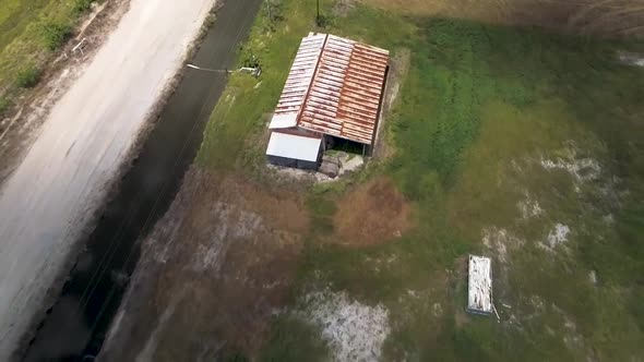 Aerial shot of old structure with rusted metal roof on farm land