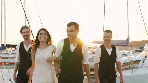 Newlyweds and Friends of a Friend Stroll Along the Pier Where There Are a Boats