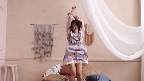 Happy Woman Jumping on Her Bed in a Cute Floral Dress