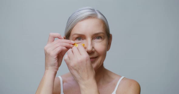 An Elderly Model Applies Patches Under Her Eyes While Smiling at the Camera