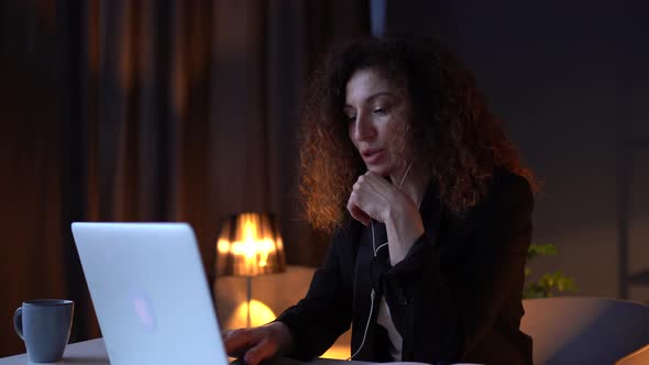 Attractive Curlyhaired Business Woman in a Business Suit Sitting Near a Laptop at a Work Table in