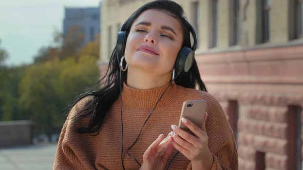 Young Carefree Woman Outdoors in City Listening Music in Headphones From Smartphone Cute Happy