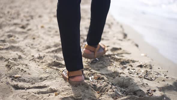 Live Camera Follows Male African American Feet in Sandals Walking on Sandy Beach with Foamy Waves