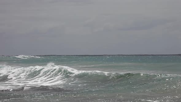 Distant waves rolling in and crashing over the rocks and beach surrounding.