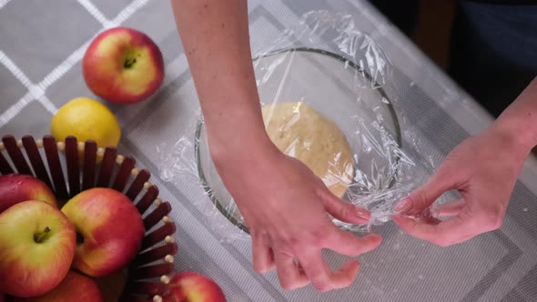 Apple Pie Preparation Series  Woman Covers Dough in Glass Bowl with Plastic Film