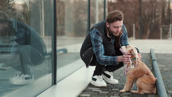 Young Man Sitting with Lovely Dog Outside Near Glass Building