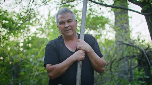 The Farmer Works with a Rake in the Garden