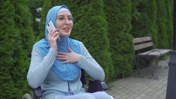 Portrait Young Muslim Woman Disabled in a Traditional Scarf Communicates on a Smartphone Sitting in