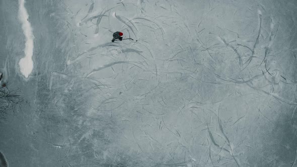 Drone looking down towards a single player playing ice hockey on a frozen pond or lake in Canada.