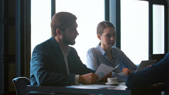 A group of employees in suits sits at a table in the office and discusses