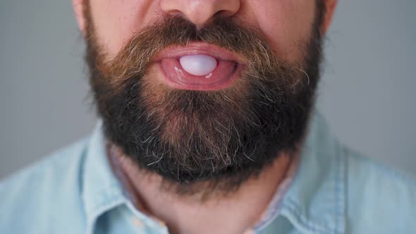 Close-up of a Bearded Man's Mouth Chewing Chewing Gum. Man Blowing Out a Bubble of Bubble Gum