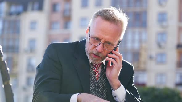 Portrait of successful senior businessman using cell phone while sitting on a bench