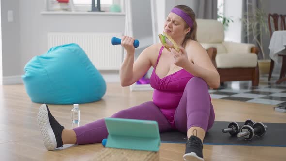 Young Obese Woman Lifting Dumbbell Smelling Sandwich