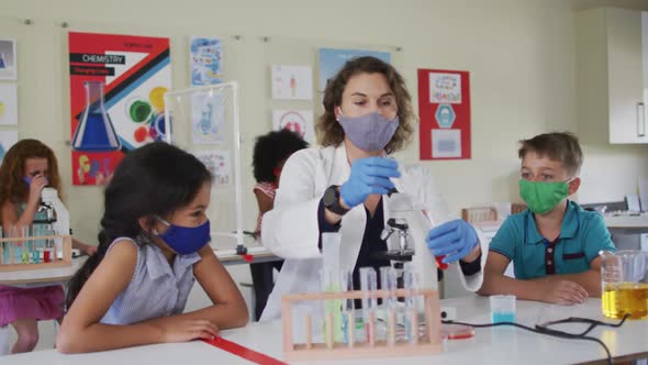 Female teacher wearing face mask and protective glasses teaching students in laboratory