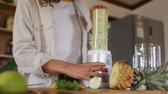 Happy mixed race woman blending health drink standing in cottage kitchen smiling