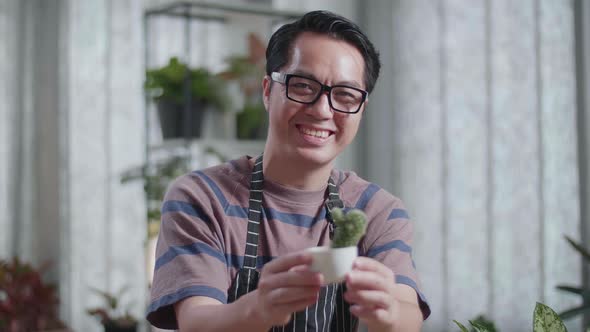 Close Up Of Smiling Asian Man Holding And Showing Cactus Plant To Camera At Home