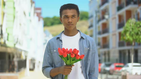 Displeased Afro-American Teen Male With Tulips Angry About Girlfriends Lateness