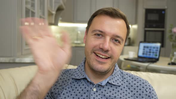 Young Adult Male Sitting on Sofa at Home Looks at Camera and Greets Colleagues Makes Live Video